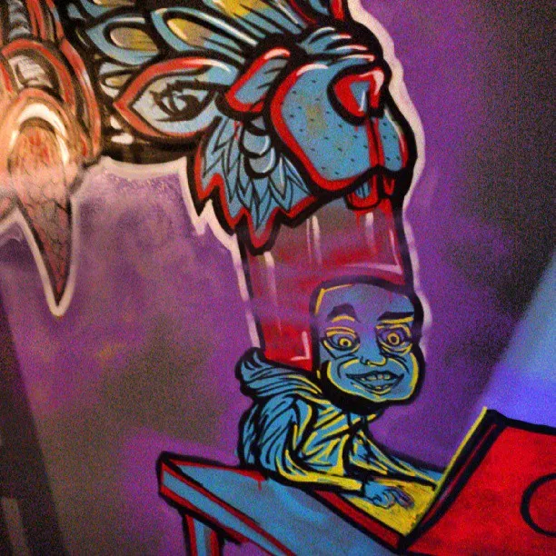 Mural of a blue character at a laptop with a massive stylized animal head emerging from its tall red hat