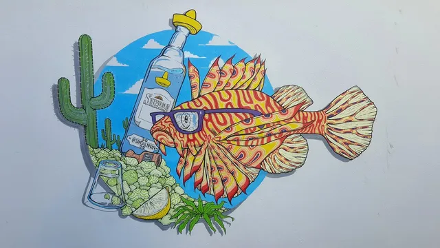 Painted cut-out of a vibrant lionfish wearing sunglasses alongside a tequila bottle, cactus, and shot glass