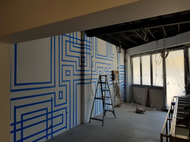 In-progress mural with blue painter's tape forming an interlocking geometric pattern on a white wall