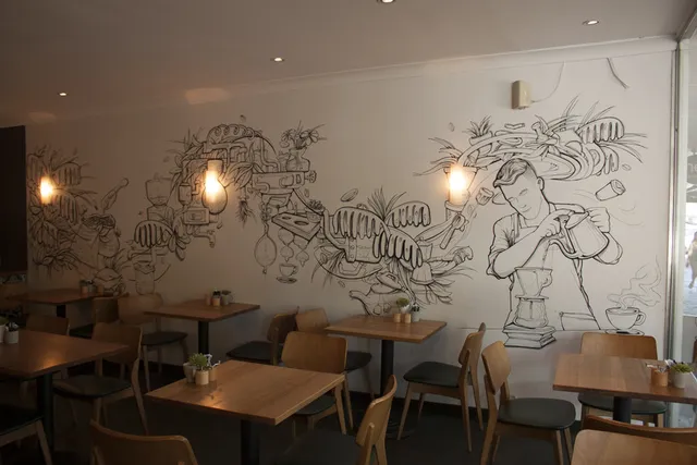 Black and white line art mural in a cafe showing a barista making pour-over coffee amidst swirling abstract brewing equipment