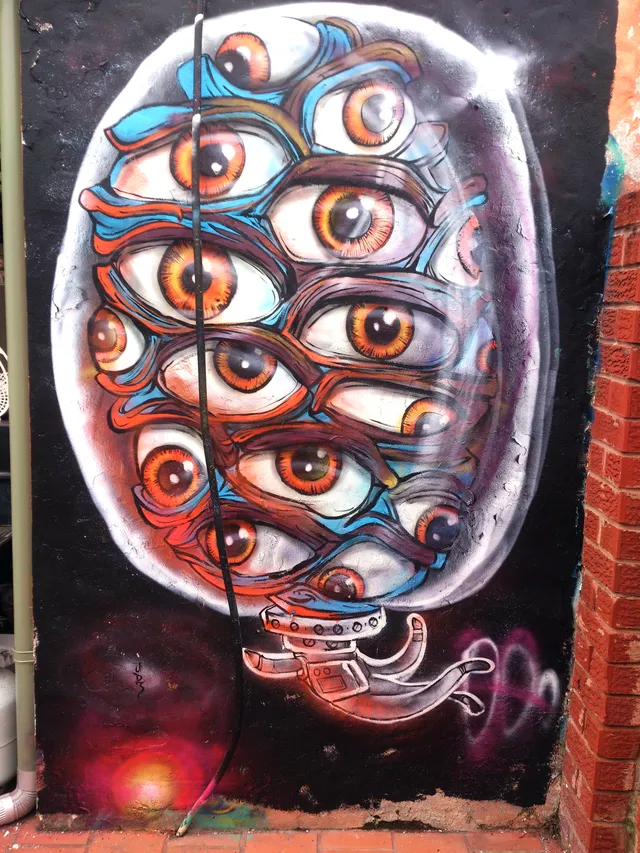Mural of an astronaut helmet filled with overlapping staring orange eyes against a dark cosmic background