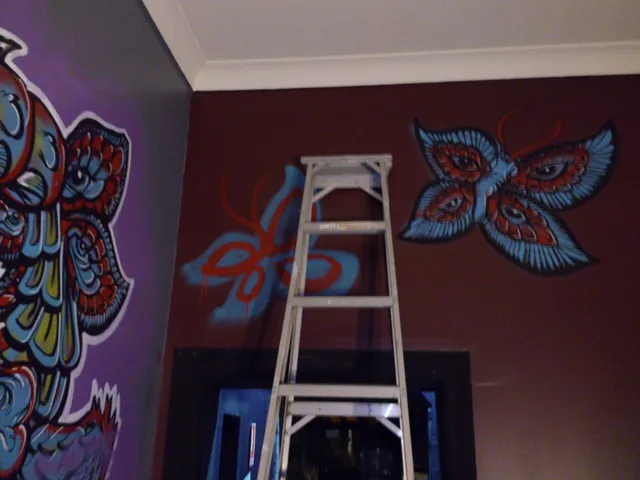 Mural in progress featuring a psychedelic blue and red butterfly with eyes on its wings near a stepladder