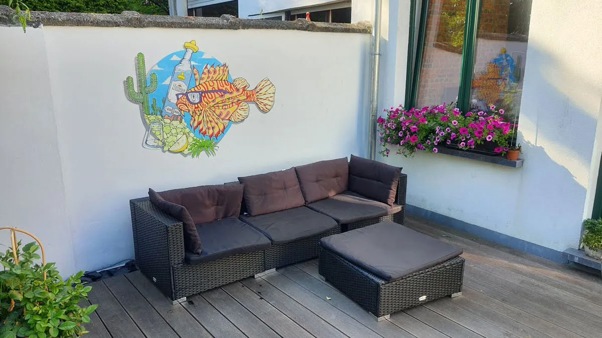 Outdoor wall mural of a lionfish wearing sunglasses next to a cactus and bottle above patio seating