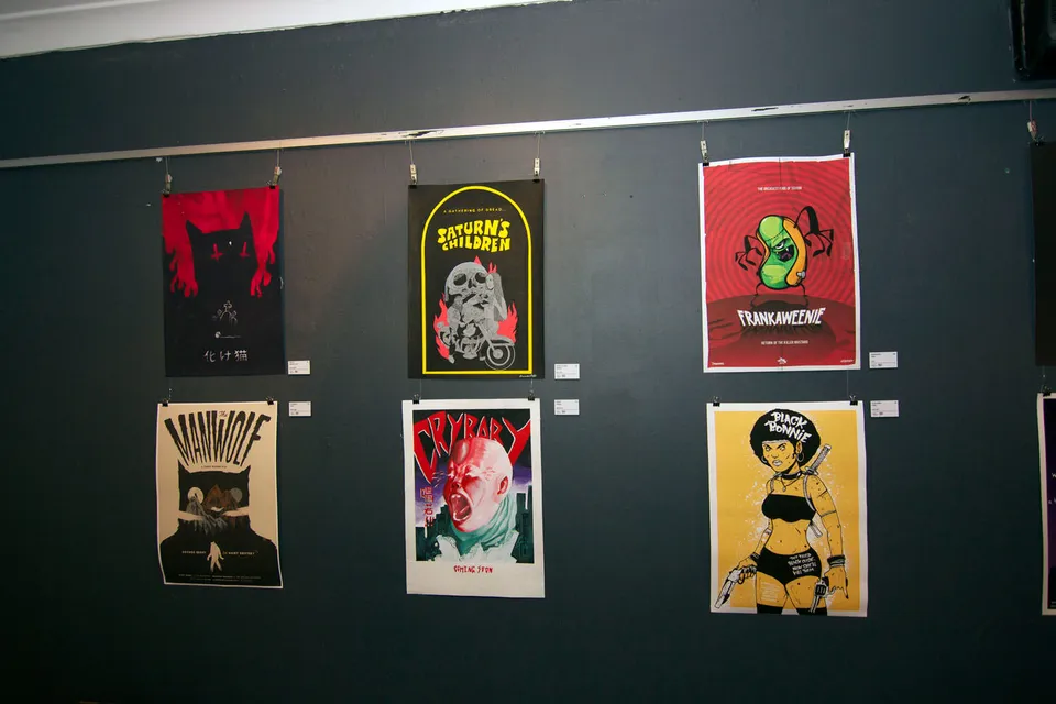 Six illustrated B-grade movie posters hanging on a dark gallery wall