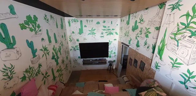 Mural across three white walls featuring line drawings of everyday objects sprouting bold green plants and cacti