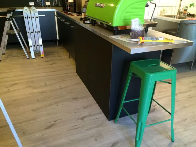 Cafe interior with a green espresso machine, green stool, step ladder, and a white line mural on the dark back wall