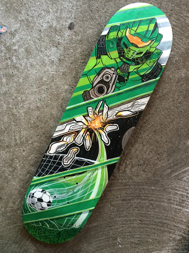 Painted skateboard deck showing a green sci-fi soldier aiming a gun, a cosmic explosion, and a soccer ball in a net