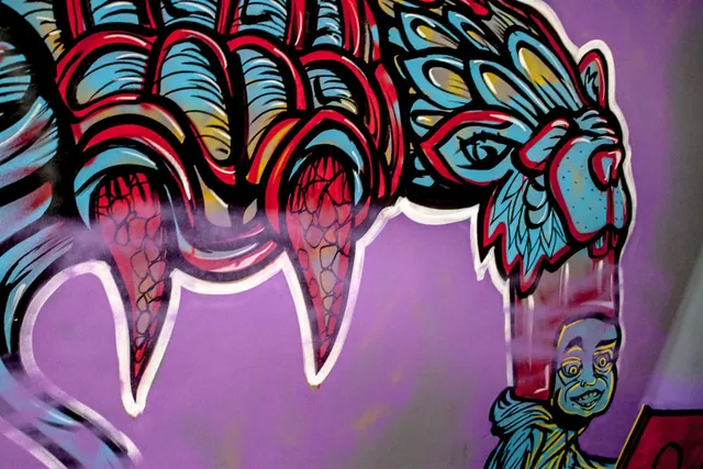 Mural detail of stylized claws and a psychedelic animal head stretching into a small human face on a purple wall