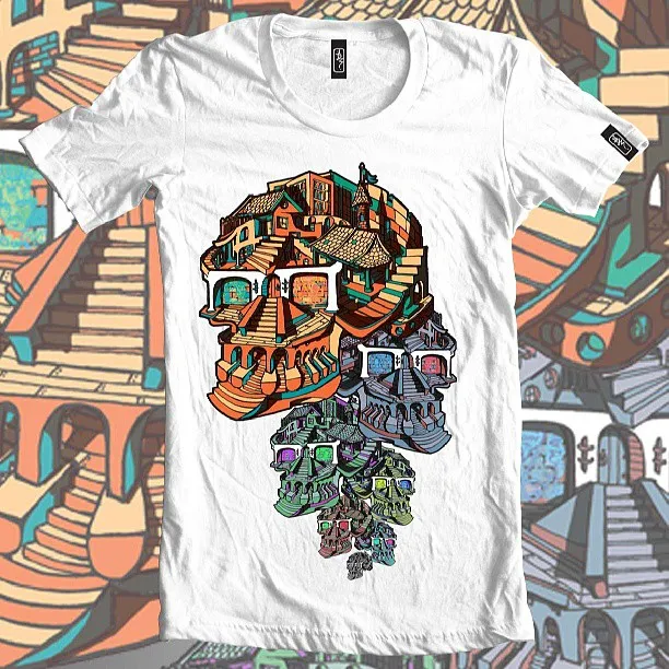 White t-shirt featuring a surreal illustration of cascading skulls formed from colorful stairs and buildings