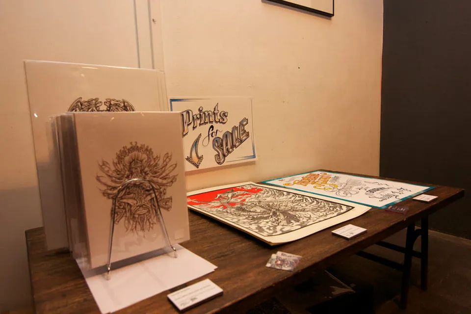 Exhibition table displaying packaged prints of totemic line work, flat posters and a Prints for Sale sign