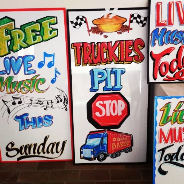 Hand-painted signs with colorful, bold lettering advertising free live music and a truckies pit stop