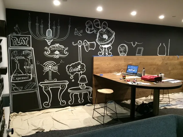 White line art mural in progress on a black office wall depicting a globe, chandelier, and shelves over a desk area