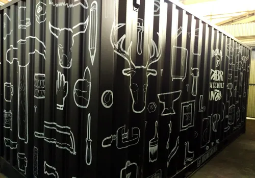 Hand-painted black shipping container covered in white line art illustrations of tools, animals, and objects