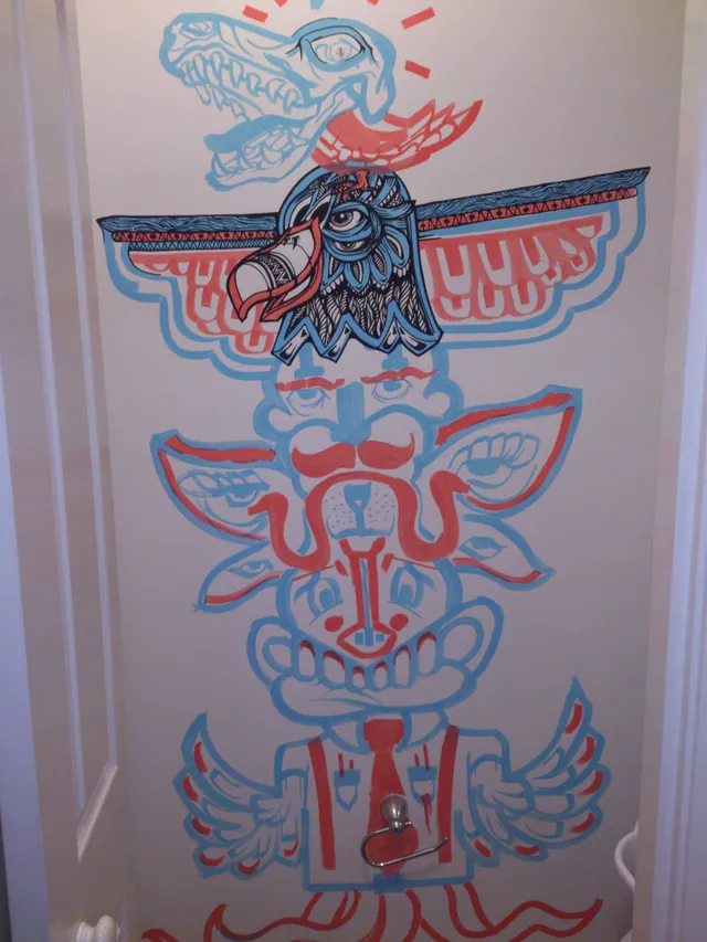 Wall mural of a stacked totem featuring a skull, eagle, and stylized faces in bold red, blue, and black line work