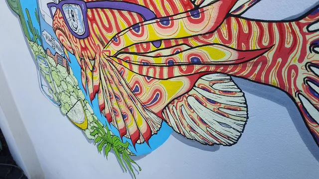 Mural detail of a psychedelic red and yellow lionfish wearing purple glasses with bold black outlines