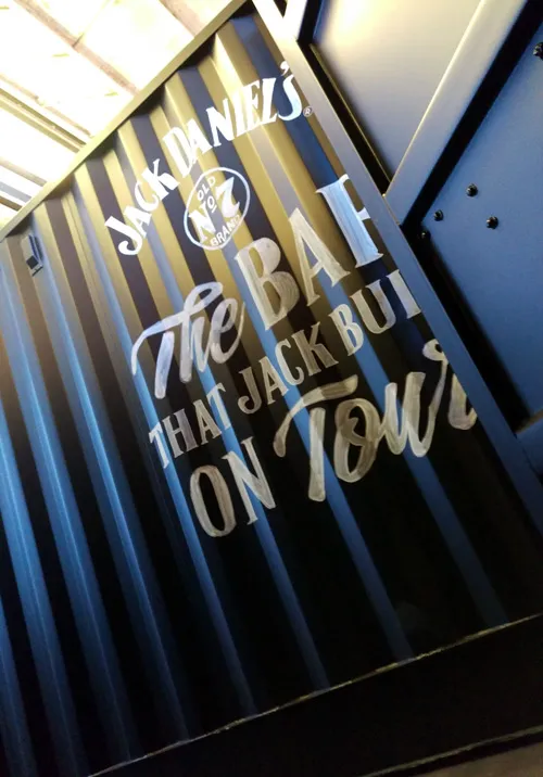 Hand-painted Jack Daniel's logo and "The Bar That Jack Built On Tour" slogan on a striped shipping container