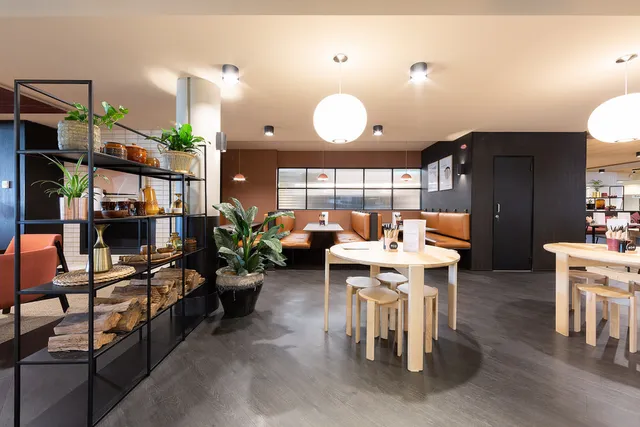Modern restaurant interior with light wood tables, orange booth seating, globe lights and black metal shelving