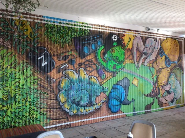 Mural on corrugated metal depicting brightly colored cartoon dinosaurs hanging out with a boombox and drinks