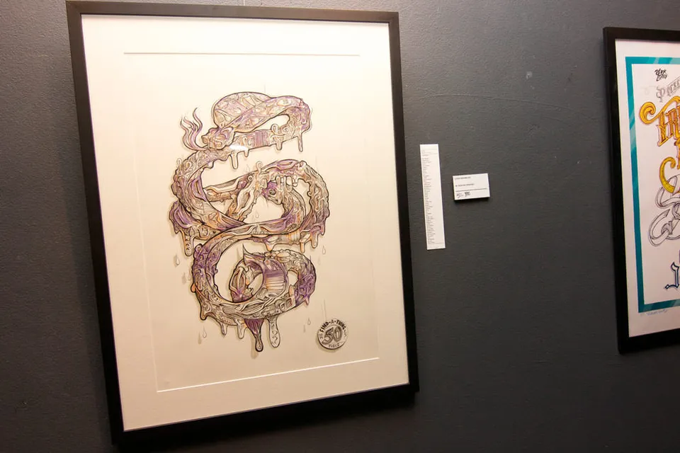 Framed illustration of a coiled, melting serpent with purple and gold details on a gallery wall