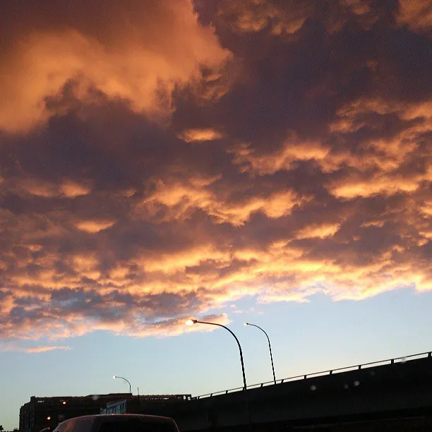 Textured orange and purple clouds at sunset above a silhouetted highway overpass and streetlights