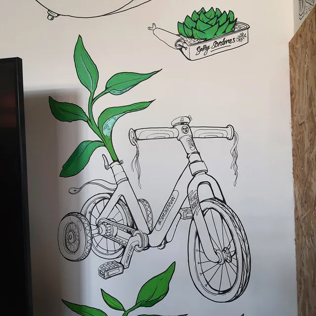 Wall mural of a black line art child's bike sprouting bright green leaves, alongside a succulent in a sardine tin