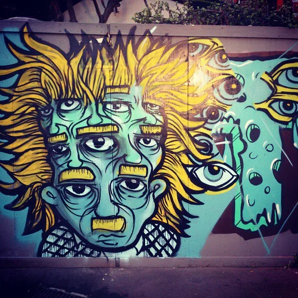 Mural of a psychedelic teal face with multiple stacked eyes and mouths and spiky yellow hair