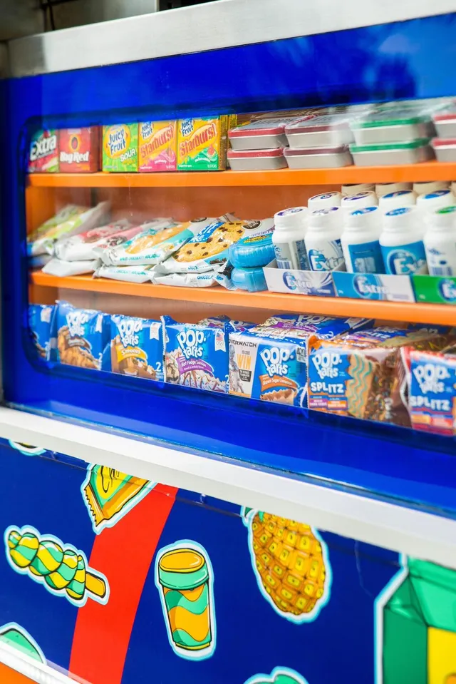 Illustrated vehicle wrap featuring colorful pop-art treats below a glass display window stocked with real snacks