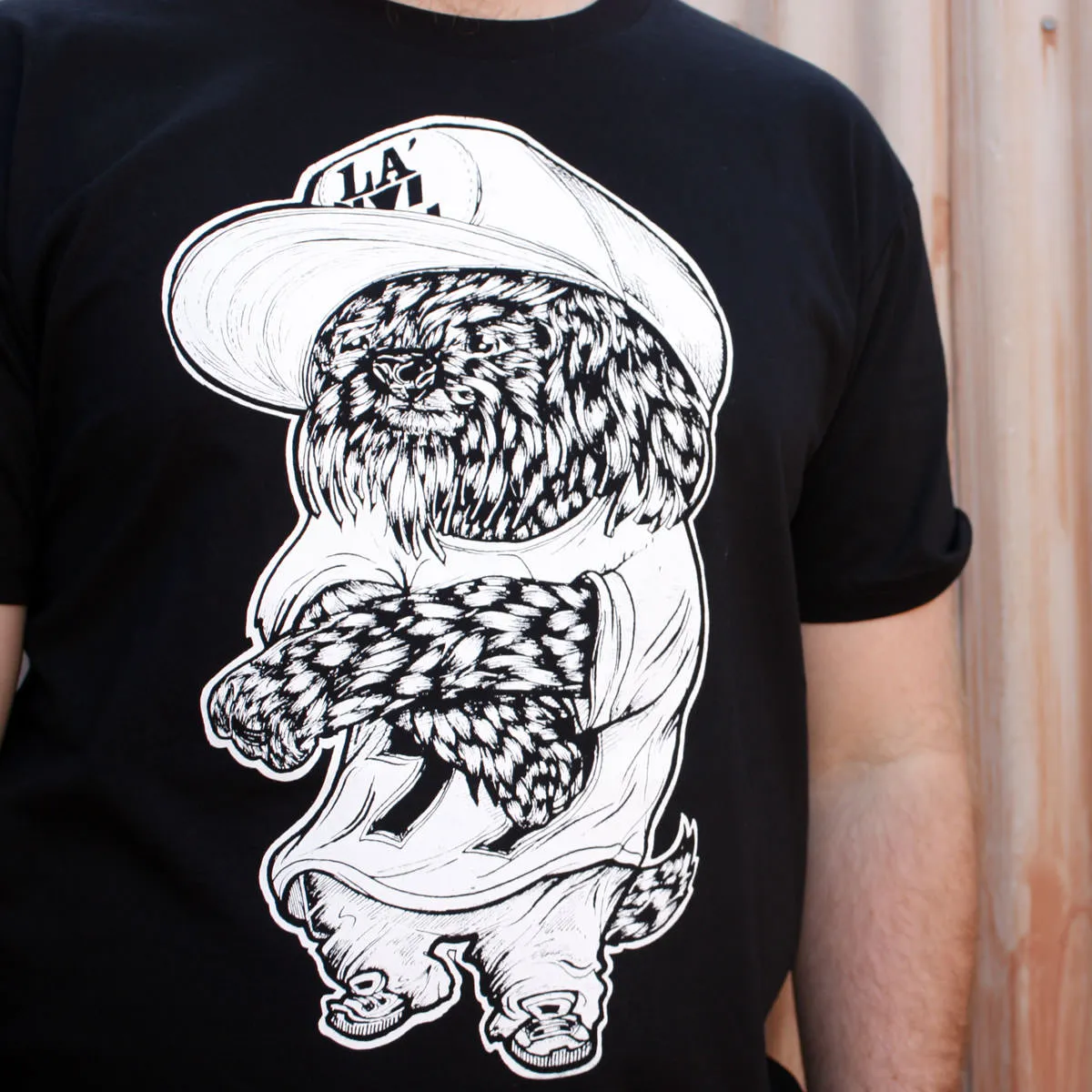 Black t-shirt featuring a bold white line illustration of a furry dog wearing a cap and sneakers with crossed arms