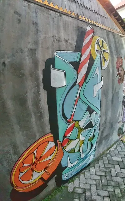 Mural on a concrete wall of a stylized, deconstructed cocktail glass with a striped straw, ice, and citrus slices