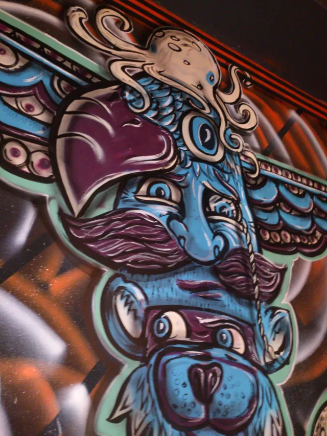 Painted mural detail of a psychedelic totem pole with stacked blue faces, a purple mustache and an octopus
