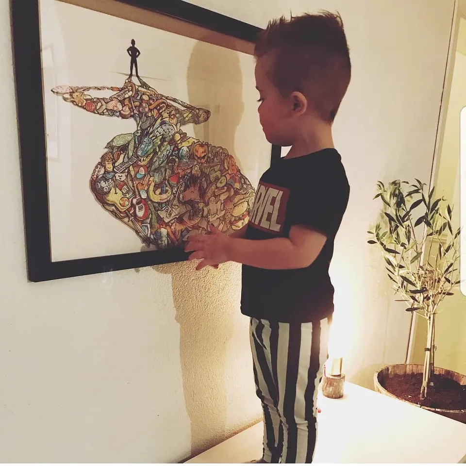 Child examining a framed illustration composed of densely packed colorful doodles with a small silhouette figure on top
