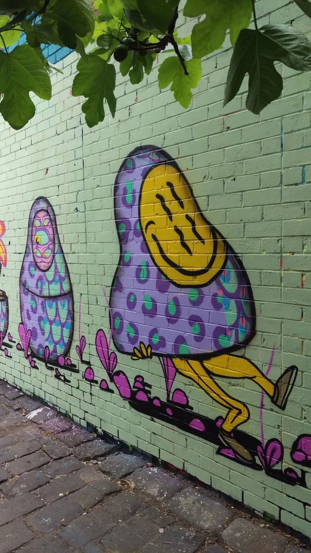 Brick wall mural of two psychedelic babushka figures, one walking with a yellow smiley face, another with multiple eyes