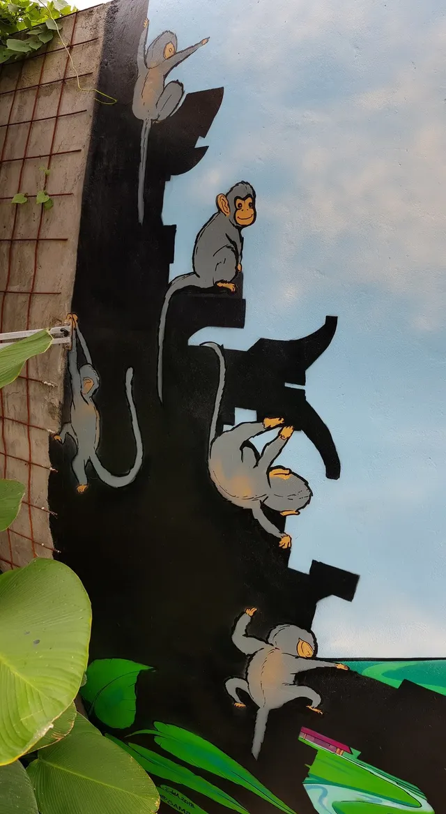 Mural of stylized grey monkeys climbing on a black silhouette of a temple structure against a painted blue sky