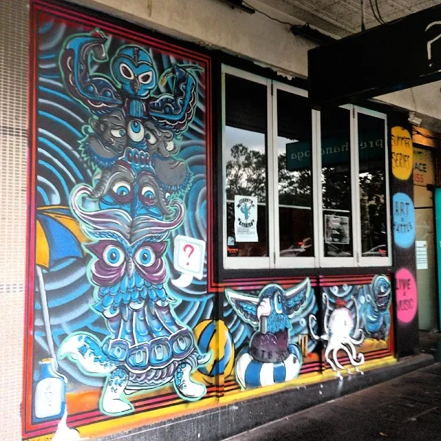 Psychedelic exterior mural depicting a blue totem of stacked animal faces, an octopus, and a bird in a life ring