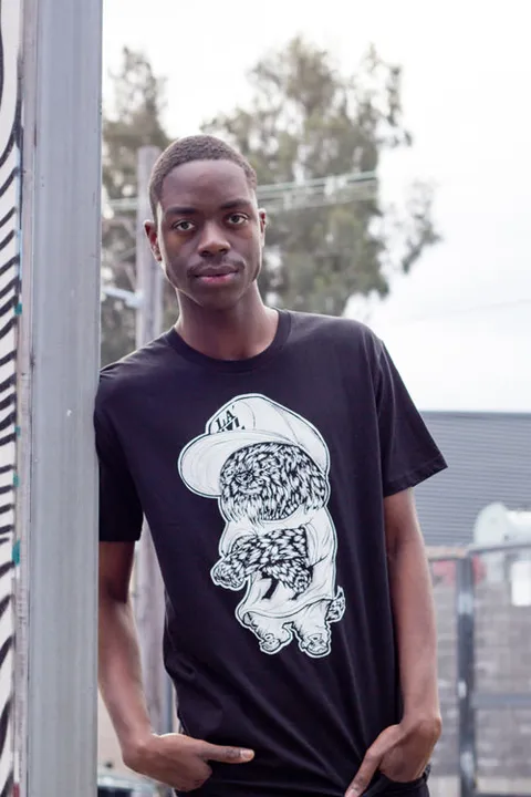 Man wearing a black t-shirt with a white line drawing of a fluffy dog in an oversized baseball cap and baggy shirt