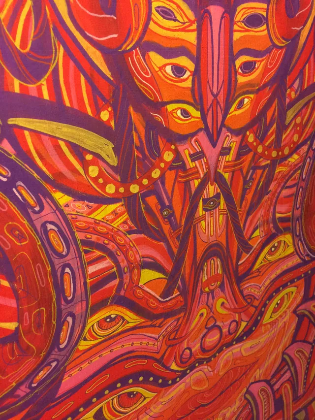Psychedelic painting of a symmetrical totemic face with multiple eyes and bold linework in red, orange, and purple