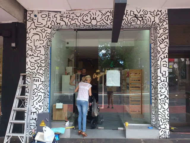 Black and white mural featuring bold interlocking line art and faces painted around a storefront entrance