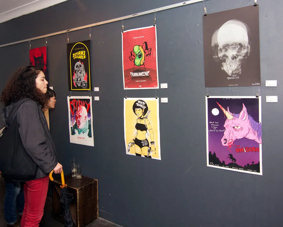 Gallery visitors viewing an exhibition of bold, colorful illustrated posters hanging on a dark wall