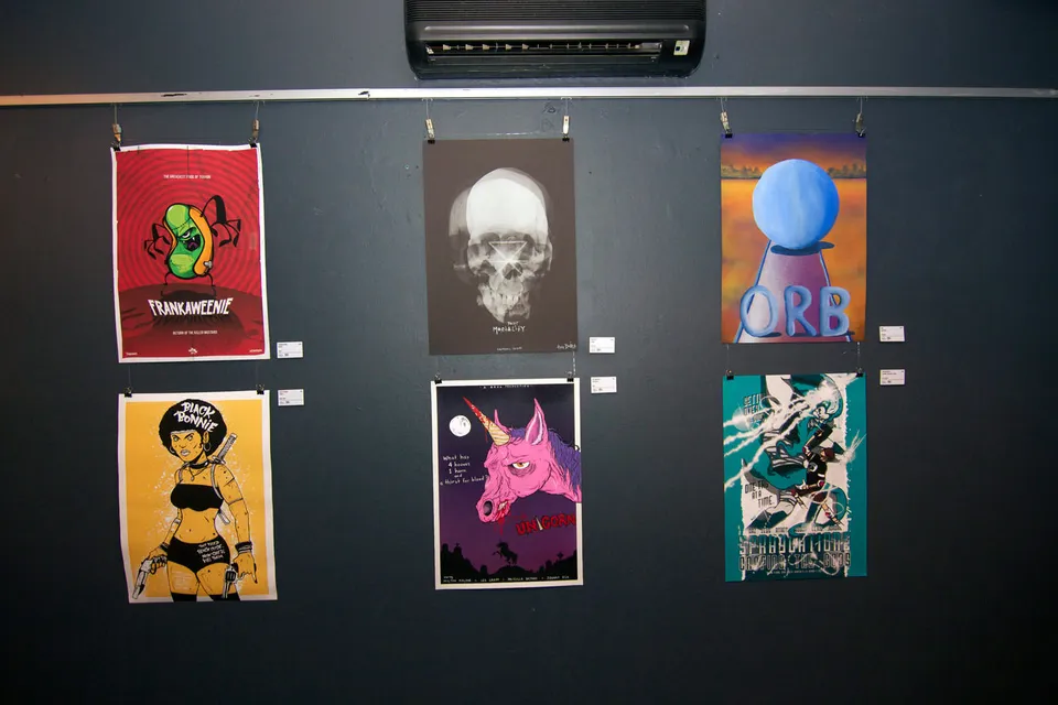 Six illustrated mock movie posters hanging on a dark gallery wall in two rows