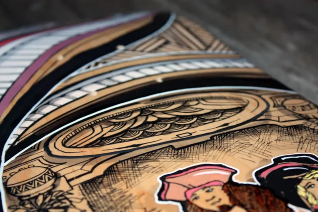 Close-up of a painted skateboard showing bold black line work, intricate geometric patterns and a pirate character