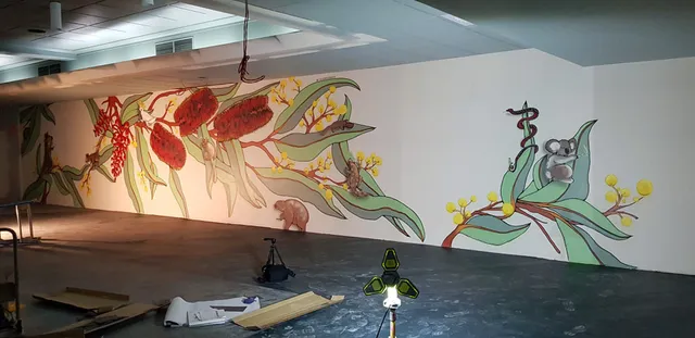 In-progress indoor mural featuring large banksia flowers, wattle, a koala, snake, and possums