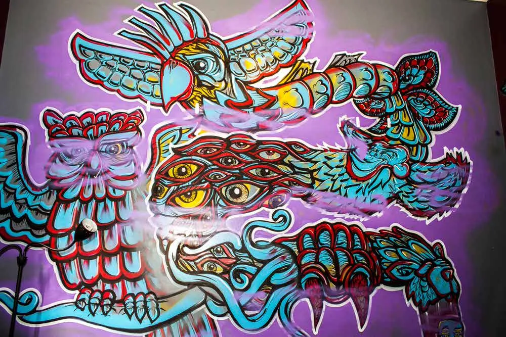 Psychedelic mural of an owl, bird, and swirling shapes with multiple eyes in bold blue and red against a purple background