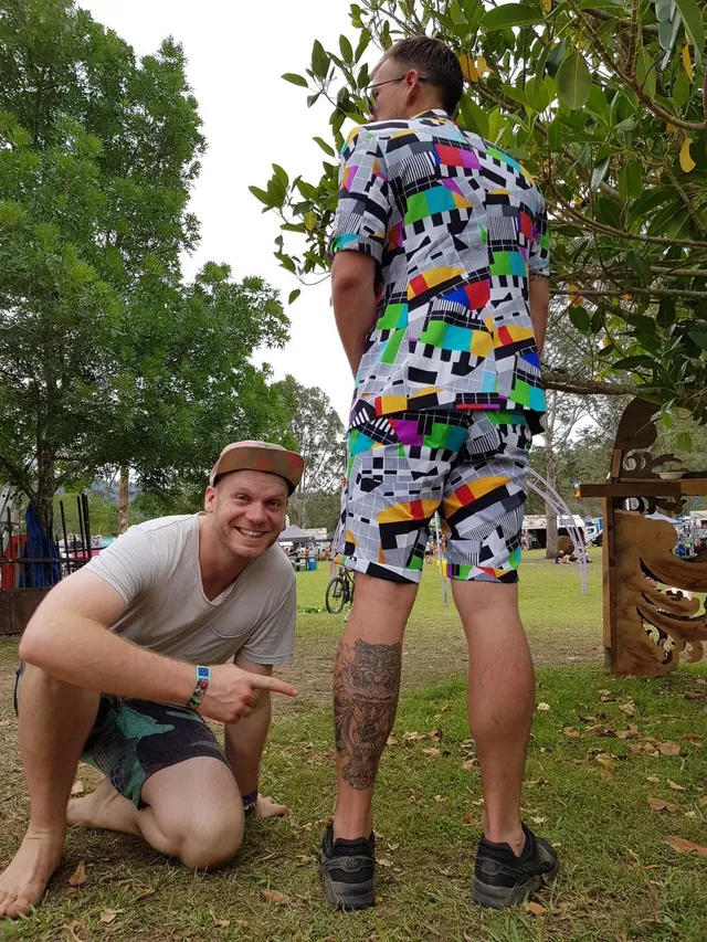 Smiling man pointing to an intricate totemic cheetah tattoo on the calf of a standing man outdoors