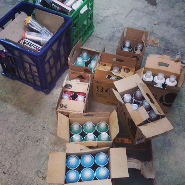 Open cardboard boxes and a blue plastic crate filled with spray paint cans on a concrete floor