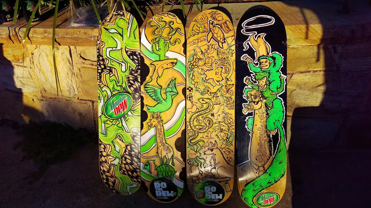 Four painted skateboards featuring totemic stacked animals, green monkeys, bold line work and Mountain Dew branding
