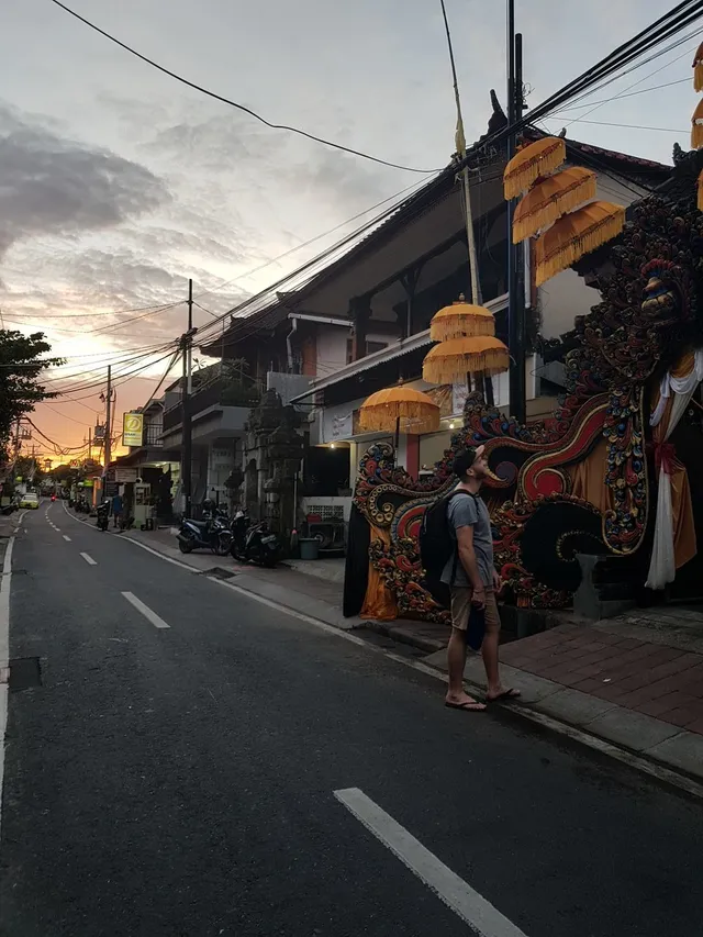 Man with a backpack on a street at sunset looking at a colorful ornate structure decorated with yellow umbrellas