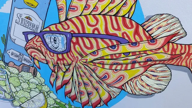 Mural of a psychedelic red and yellow lionfish wearing purple glasses next to a bottle and pile of hops