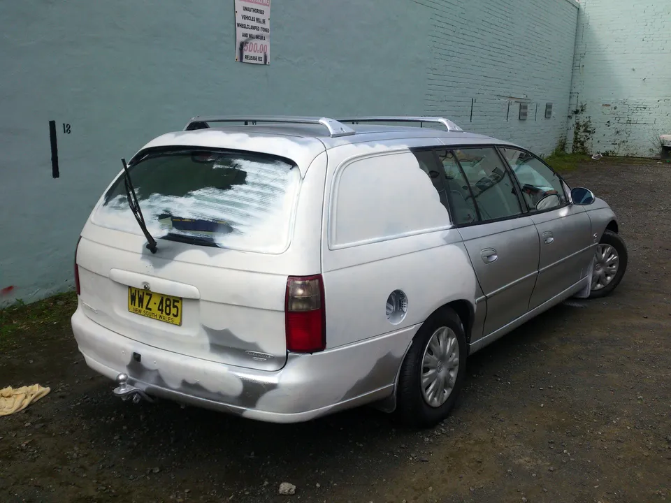 Silver station wagon with its rear half and back window covered in white primer in preparation for a painted mural