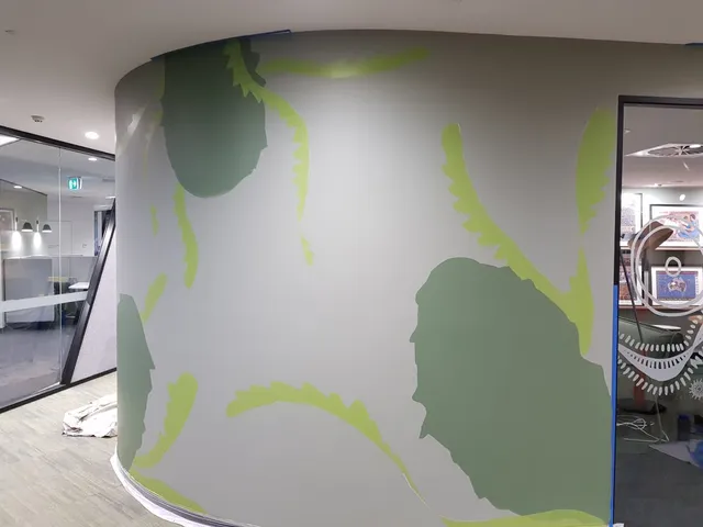 In-progress mural on a curved office wall showing base layers of dark and light green organic shapes