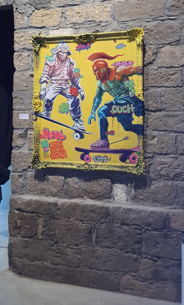 Framed yellow painting of a skeletal samurai and spartan warrior riding skateboards surrounded by graffiti text